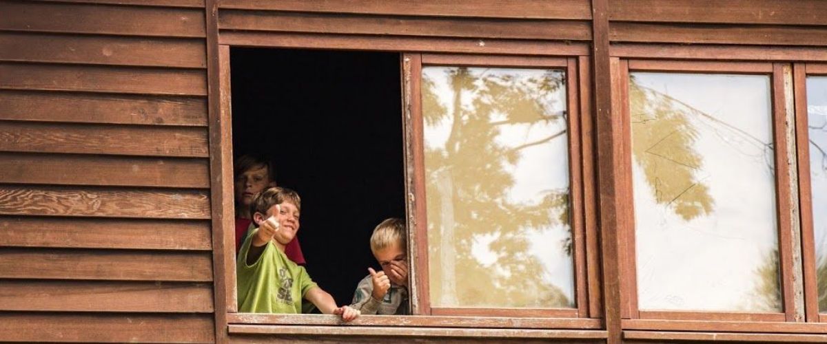 Drie scoutsleden kijken door het raam van een blokhut