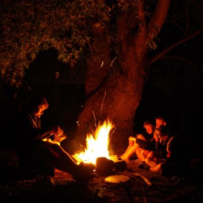 Scoutsleider leest voor aan drie leden rond het kampvuur
