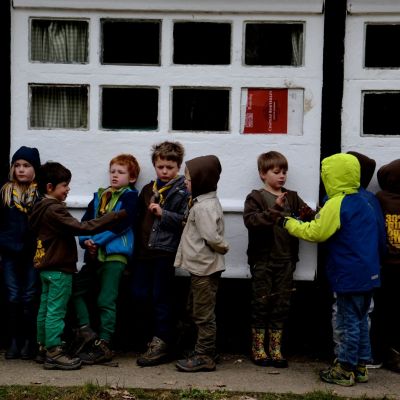 kapoenen in regenkledij tegen de muur van een lokaal