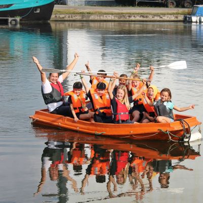 Kinderen met begeleider die met reddingsvesten in een raft zitten.