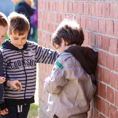 Drie jonge scouts staan geheimzinnig te doen aan een muur. Een leunt tegen de muur. Wordt die gepest?