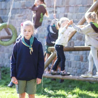 op de achtergrond spelende gidsen op een gesjorde speeltuin. Er een triest kijkende gids. 