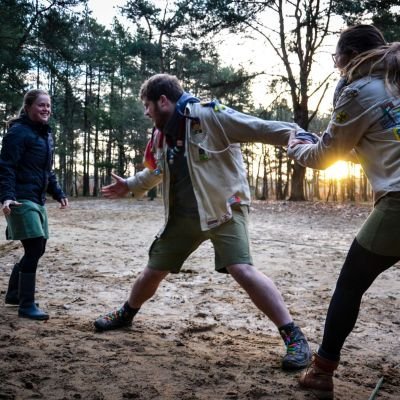 Drie scoutsleiders spelen een spel en trekken aan elkaars armen