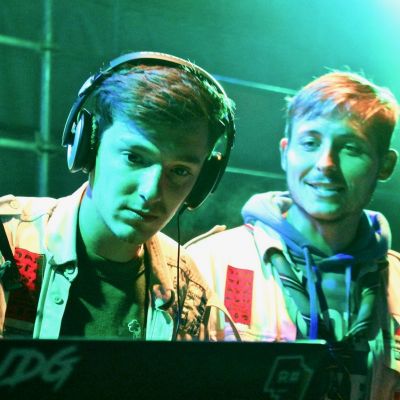 Twee scoutsleiders in uniform en met hoofdtelefoon op zijn DJ's op een feest.