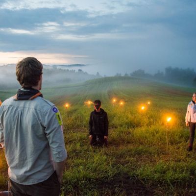 Adriaan Beernaert In een glooiend landschap bij zonsopgang zit een geblinddoekte scout op zijn knieën klaar voor zijn totem. Een leider spreekt hem toe.