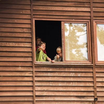 Drie scoutsleden kijken door het raam van een blokhut