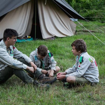 Hana Reynaert Een leider en twee leden praten al zittend voor hun tent.