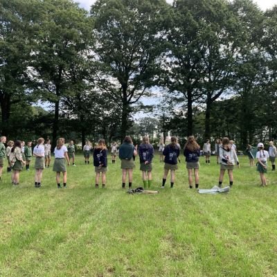 Scoutsgroep staat in een grote kring op een grasveld
