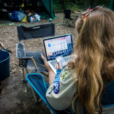 een leidster zit midden het bos voor een tent op haar laptop te werken