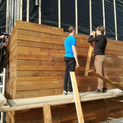 3 mannen timmeren planken tegen een lokaal