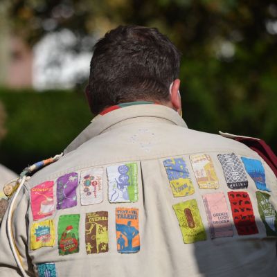 Leider heeft uniformhemd aan. Op het hemd is een hele verzameling jaarkentekens genaaid.