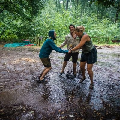 Twee meisjes en een jongen dansen in de regen met hun voeten in de modder.