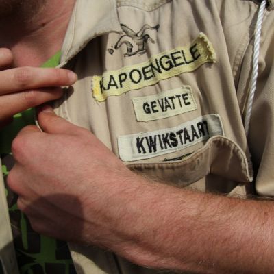 een leider met totem kapoengele gevatte kwikstaart knoopt zijn scoutshemd toe