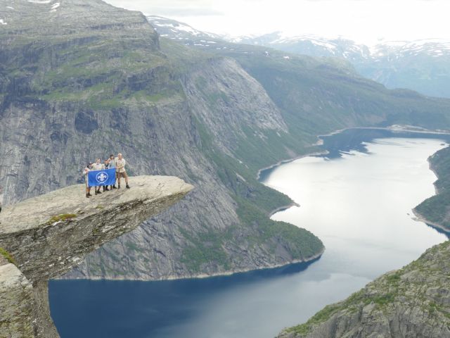 Jins staan met een vlag in de handen op een overhellende rots in Noorwegen
