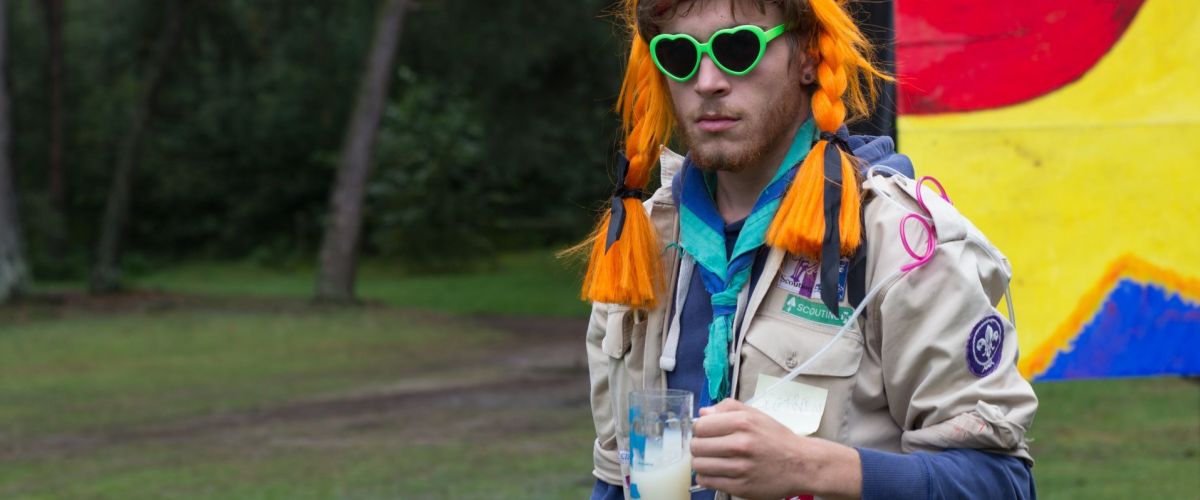 Scoutsleider in uniform met drankje in zijn hand.