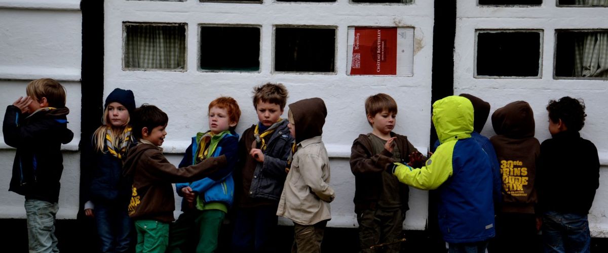 kapoenen in regenkledij tegen de muur van een lokaal