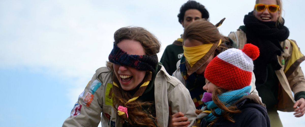 Vijf scouts en gidsen op een rij. Twee zijn geblinddoekt.