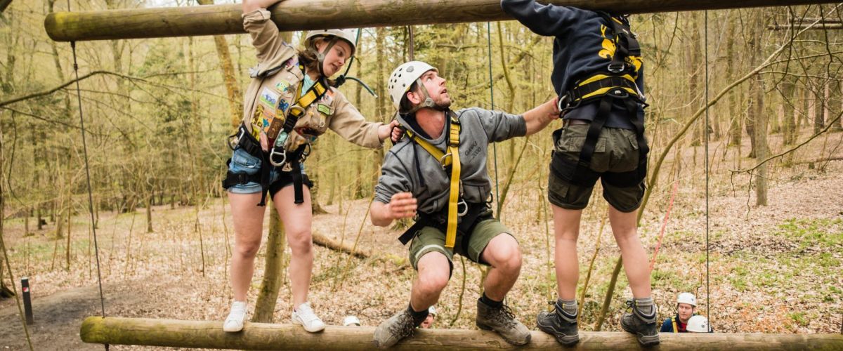 Drie leiders zijn beveiligd en helpen elkaar op het touwenparcour op Jeugdverblijf De Kluis.