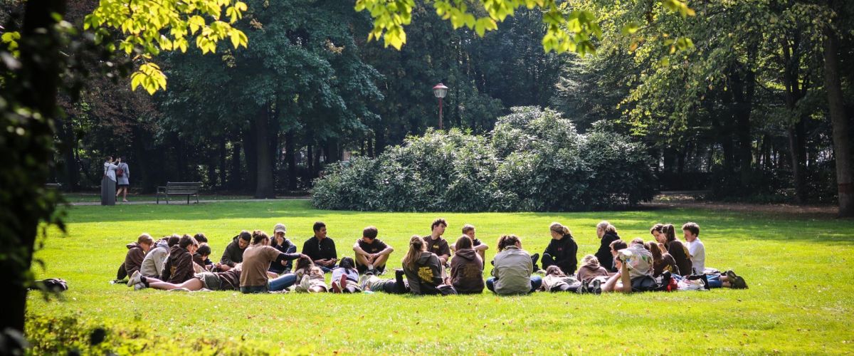 Een scoutsgroep in een cirkel zit op het gras onder de zon in het park