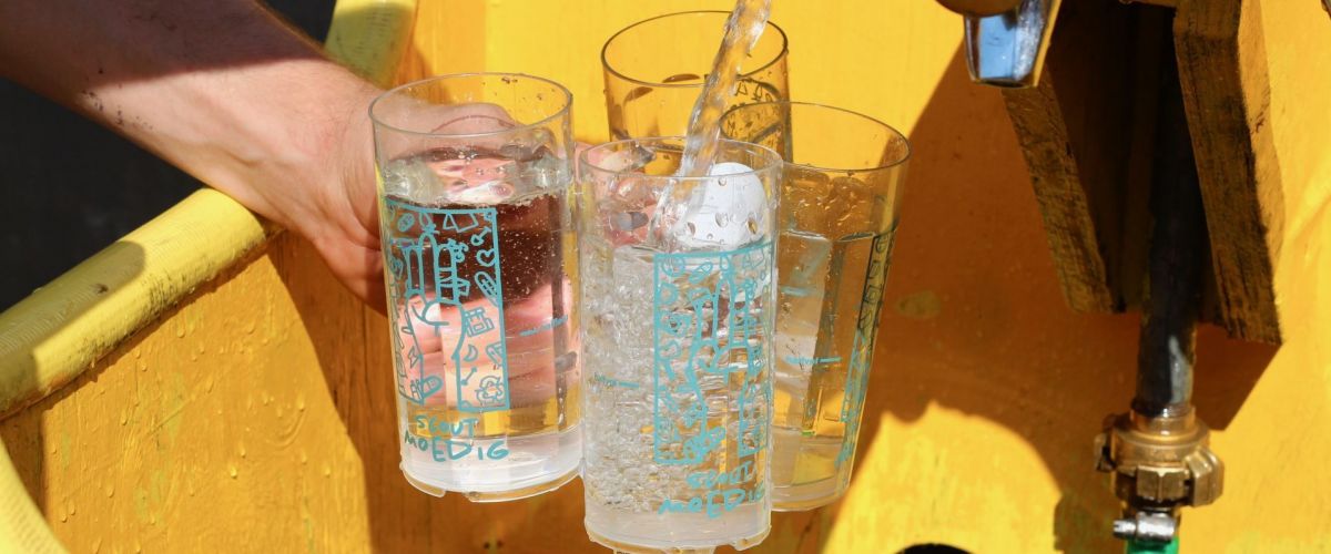 Drie Herfstontmoetingsbekers worden aan een kraantje gevuld met water. Drie Herfstontmoetingsbekers worden aan een kraantje gevuld met water.