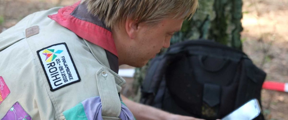 Petra Delee Een leider zit in het bos naast een boom op zijn gsm te kijken