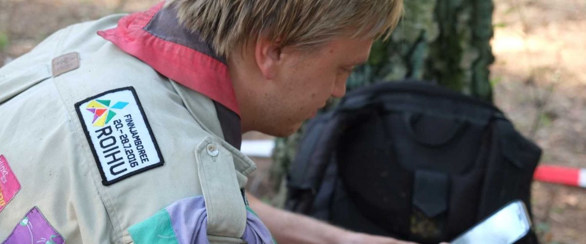 Een leider zit in het bos naast een boom op zijn gsm te kijken