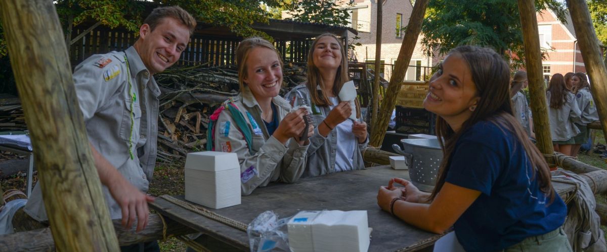 scouts en gidsen aan een gesjorde eettafel.