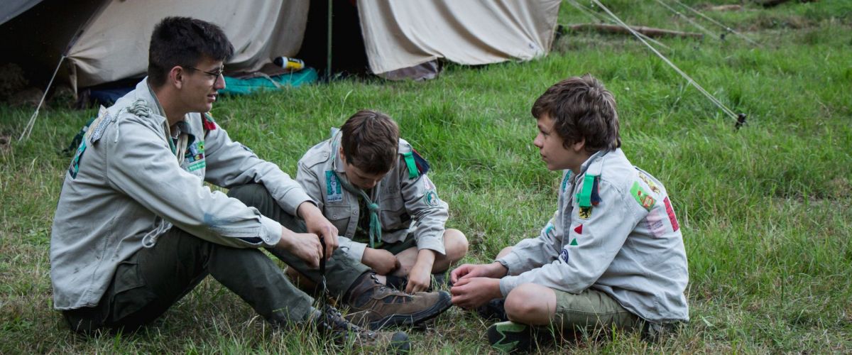 Een leider en twee leden praten al zittend voor hun tent.