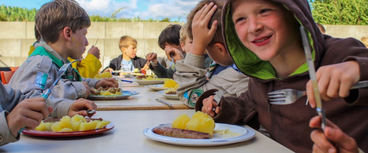 Welpen zitten aan gesjorder tafel te eten op kamp