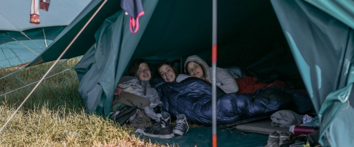 tent met 3 scoutsmeisjes, boven de tent hangen kleren te drogen