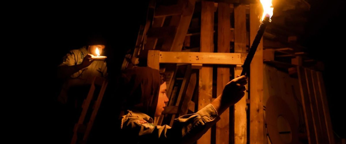 een jonggiver in het donker met een fakkel bij een houtstapel