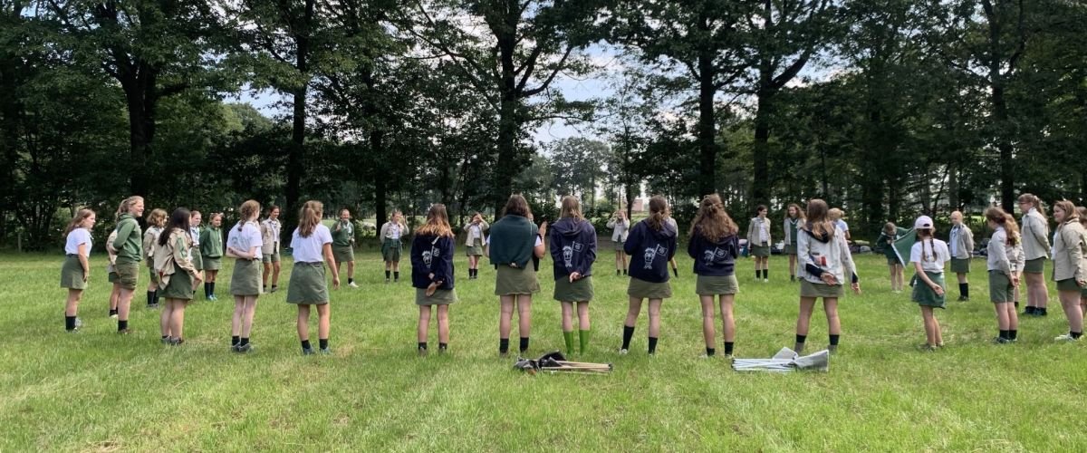 Scoutsgroep staat in een grote kring op een grasveld