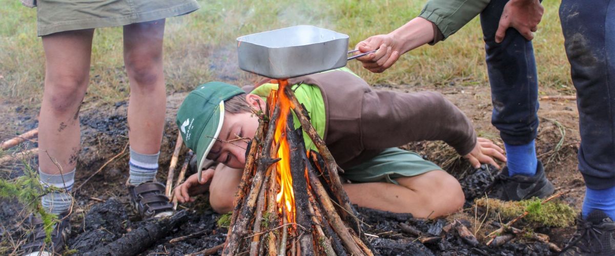 3 scouts rond houtvuur, ze blazen om vuur aan te wakkeren