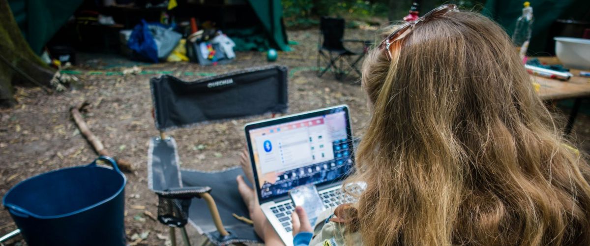 een leidster zit midden het bos voor een tent op haar laptop te werken