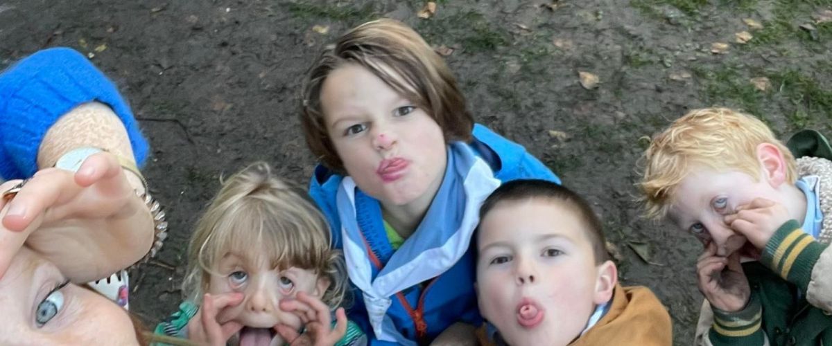 een leiding kijkt in de lens en doet de scoutsgroet. Kapoen kijken mee en trekken gekke bekken.