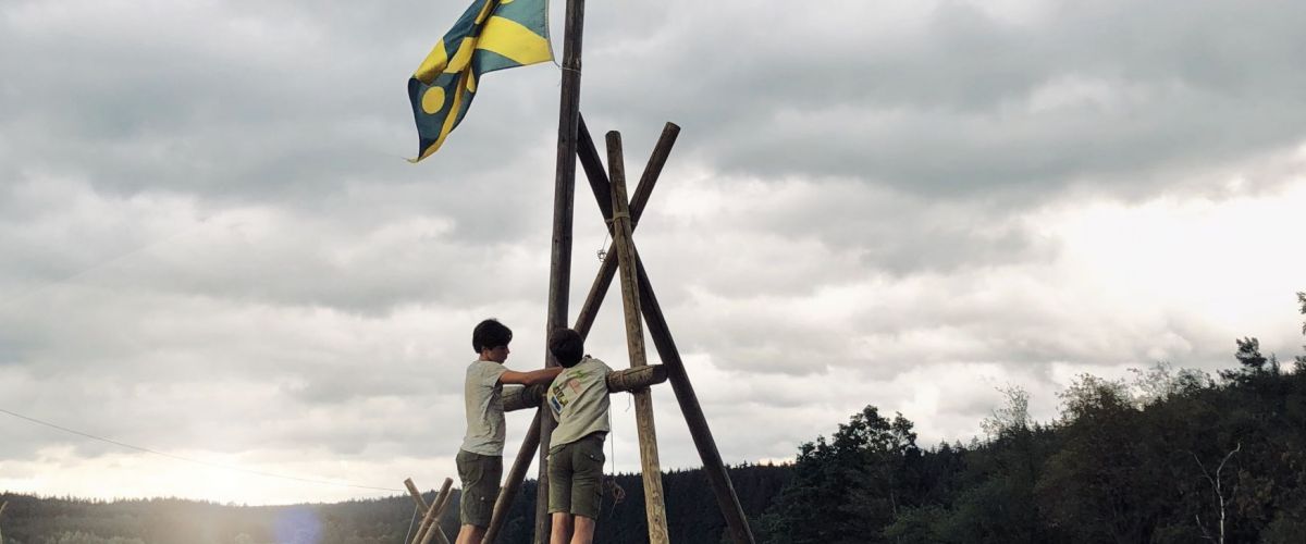 twee jongens staan op een driepikkel en plaatsen er een vlaggenmast op