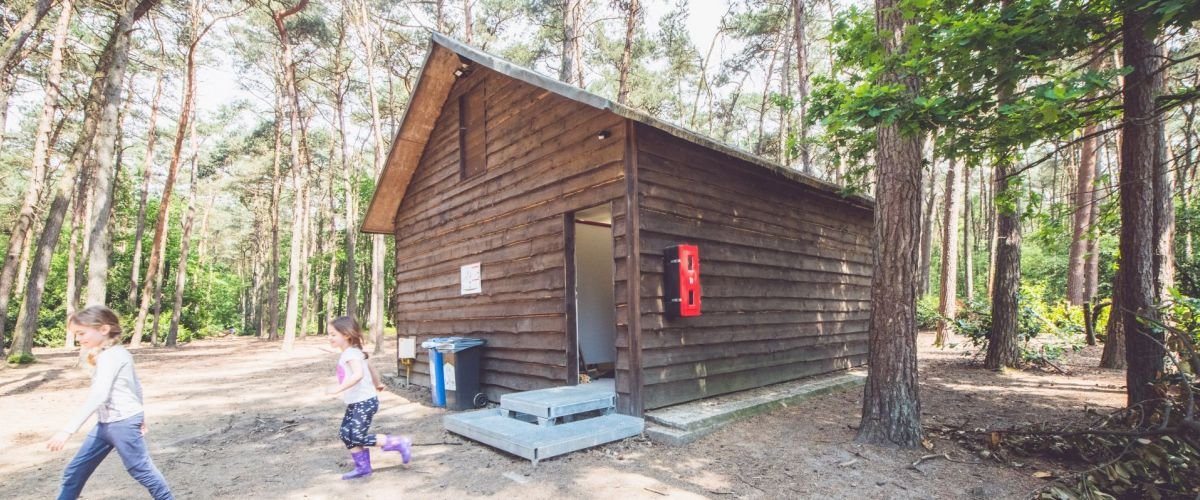 Dries Luyten Twee kinderen die naar buiten zijn gekomen uit een blokhut in een bos.