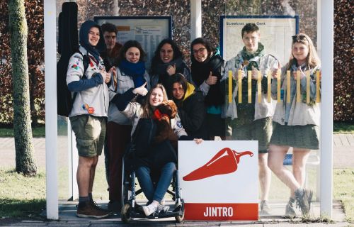 Een groep leiding, eentje in een rolstoel, vult een bushok en poseert, duim omhoog, met het Jintrobord.