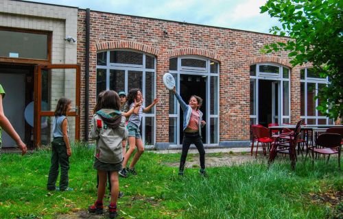 Leden spelen in het gras voor hun scoutslokaal