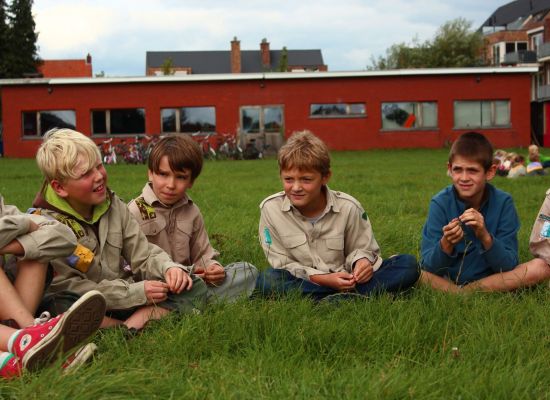 Welpen zitten voor het lokaal in kleermakerszit in het gras in een kring