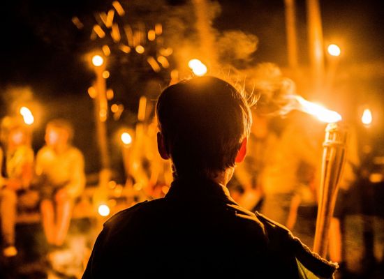 scout, met de rug naar de lens hij kijkt naar een brandende fakkel.