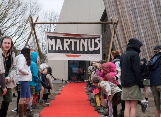 Gidsen staan aan beide zijden van een rode loper. De loper leidt naar de inkom van het nieuwe lokaal.