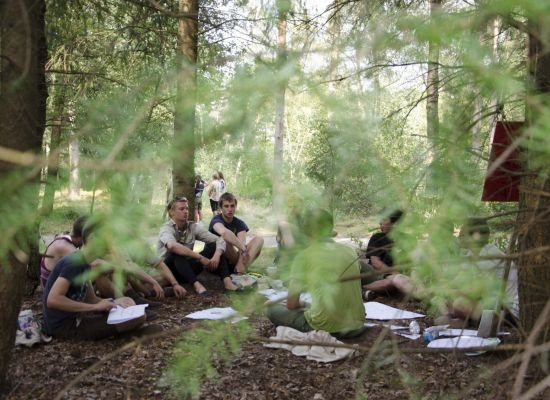 scouts zitten op de bosgrond, ze lijken een heuse vergadering te houden in het bos.