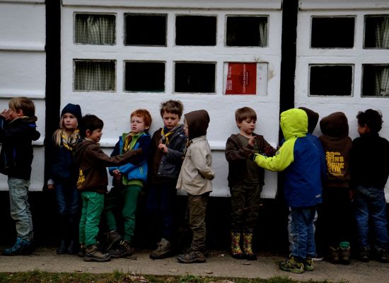 kapoenen in regenkledij tegen de muur van een lokaal