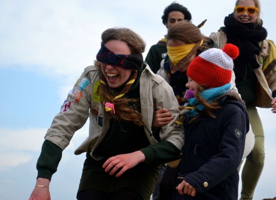 Vijf scouts en gidsen op een rij. Twee zijn geblinddoekt.