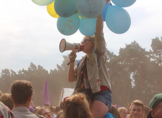 Meisje met megafoon en tros ballonnen zit op schouders van jongen.