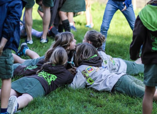 Vier leden in uniform liggen, met hun armen in elkaar gehaakt, in het gras te spelen.