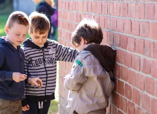 Drie jonge scouts staan geheimzinnig te doen aan een muur. Een leunt tegen de muur. Wordt die gepest?