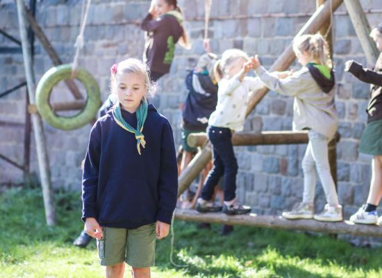 op de achtergrond spelende gidsen op een gesjorde speeltuin. Er een triest kijkende gids. 