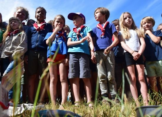 groepje scouts en gidsen met rood-witte das staan klaar om een spel te starten. 